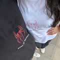 Two people wearing shirts with spider logos on a sidewalk.