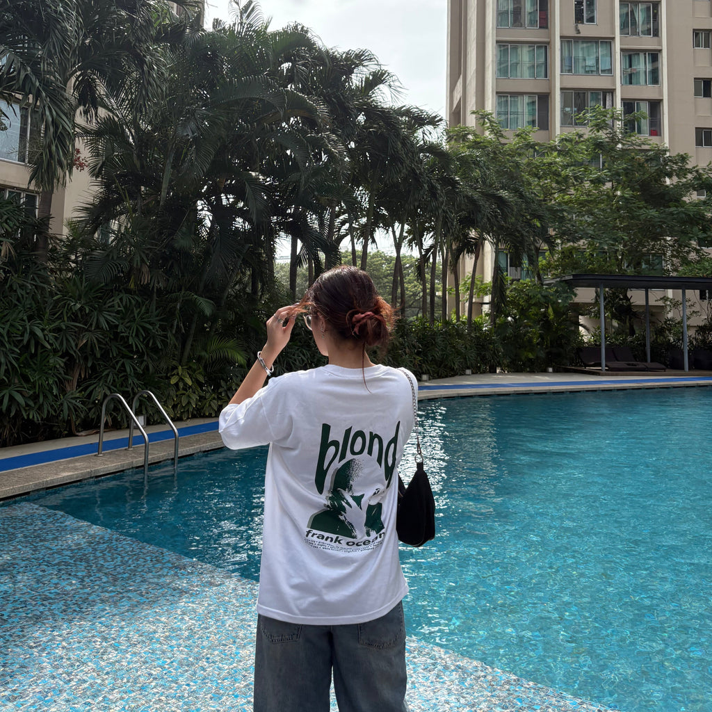 Person standing by a pool with tall buildings and trees in the background