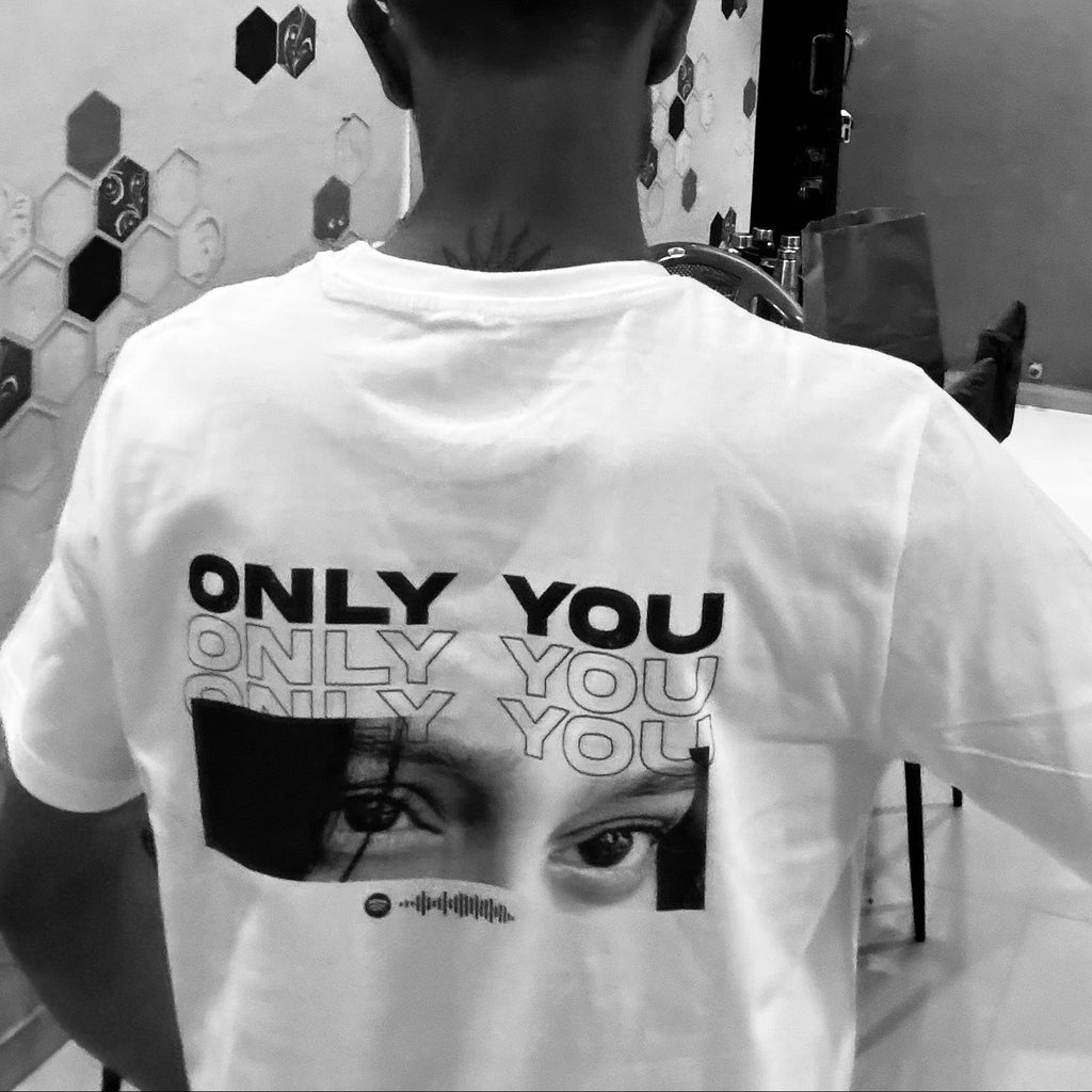 Person wearing a white t-shirt with a graphic design and text in a bathroom setting.
