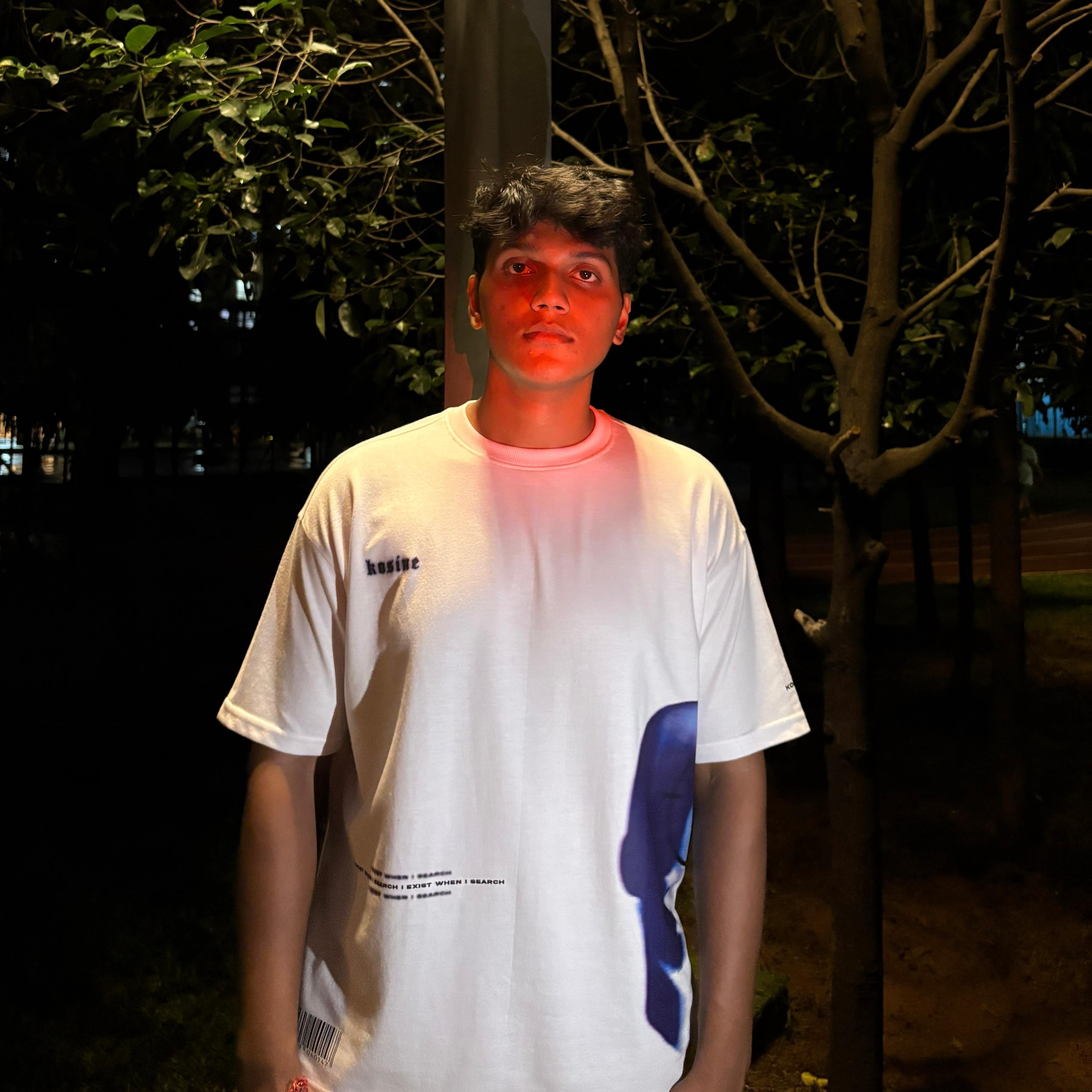 Person wearing a white t-shirt with a blue design in a dark outdoor setting