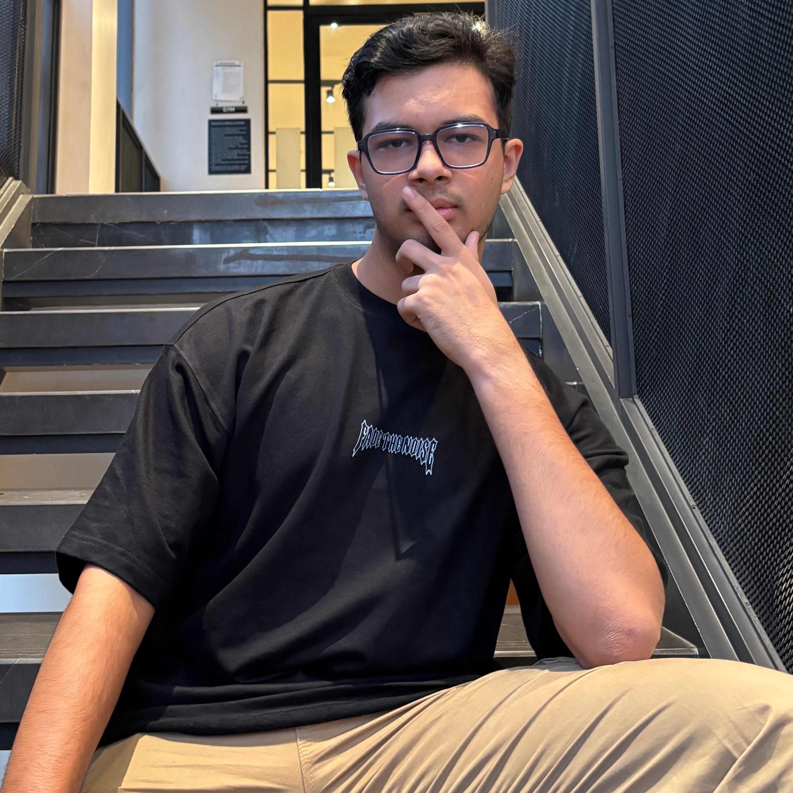Man wearing a black t-shirt with text sitting on stairs indoors