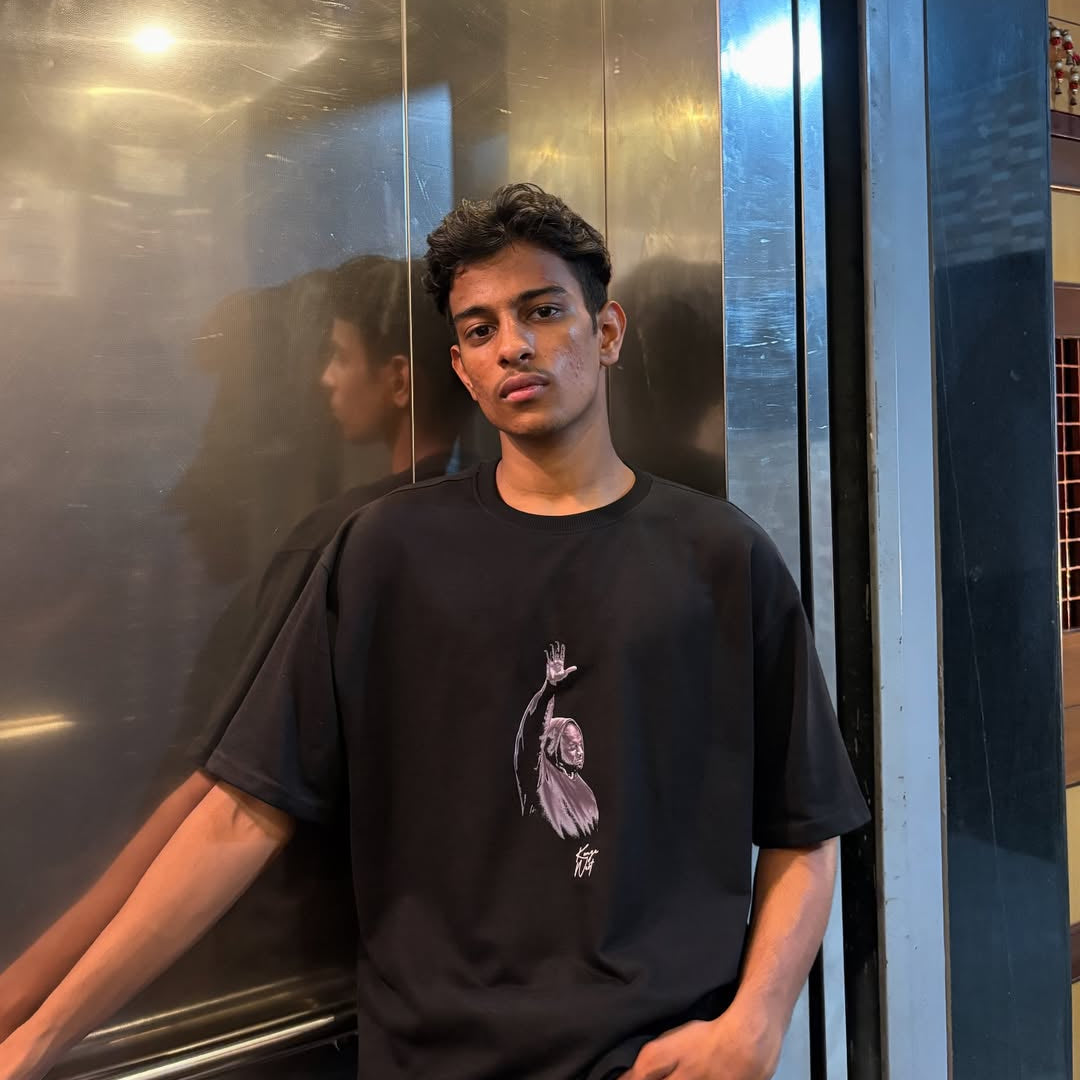 Person wearing a black t-shirt with a graphic design, standing in front of a reflective surface.