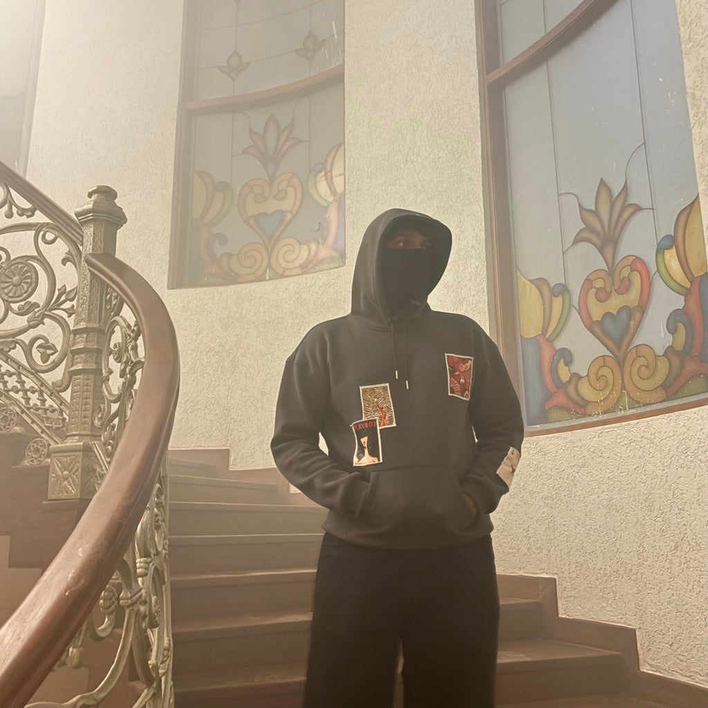 Person wearing a hoodie with patches in a foggy stairwell with decorative windows.