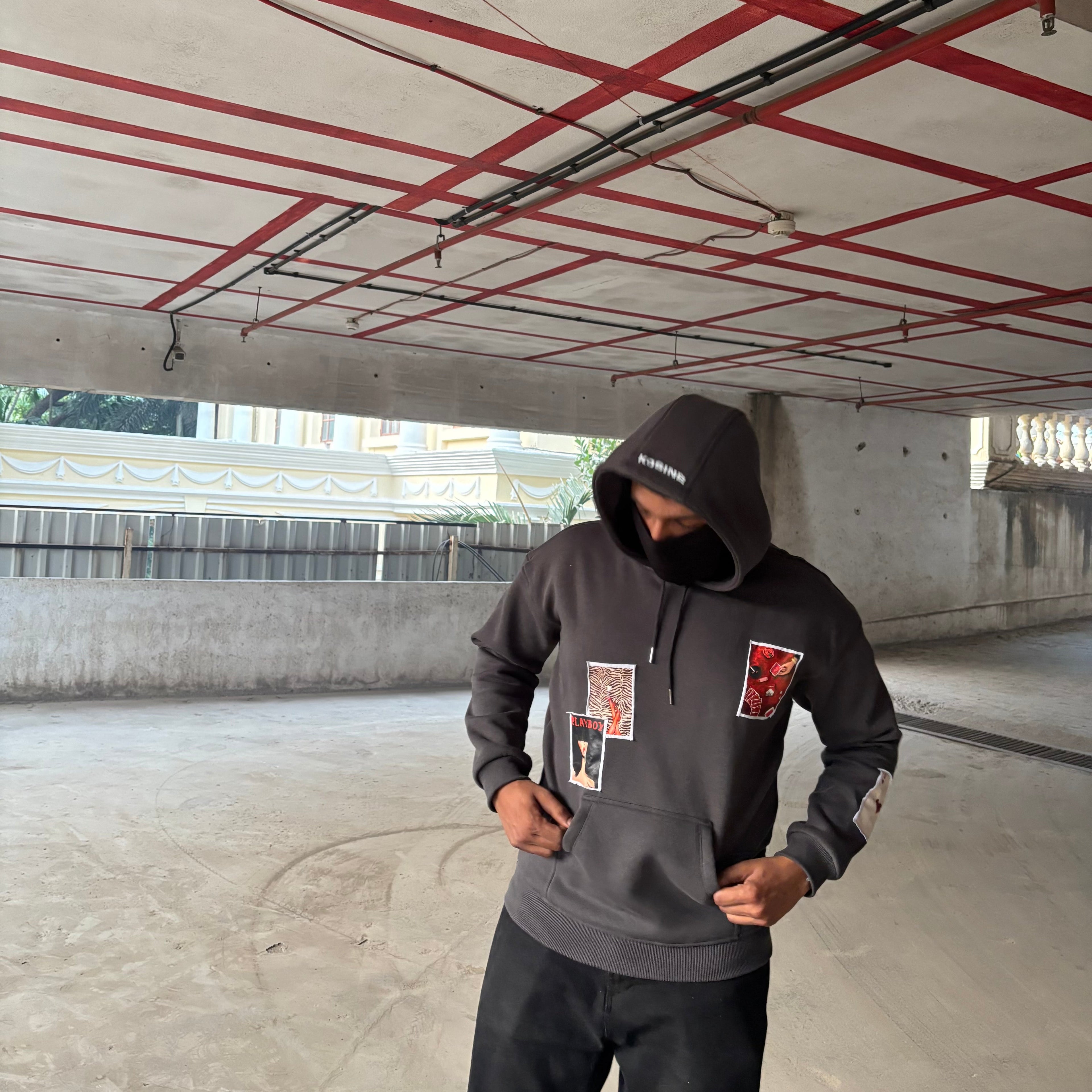 Person wearing a dark hoodie with graphic designs in an indoor setting