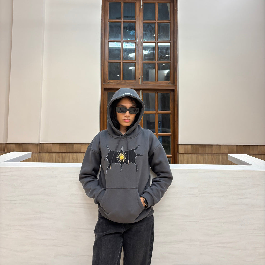 Person wearing a gray hoodie with a logo in a room with a large mirror.
