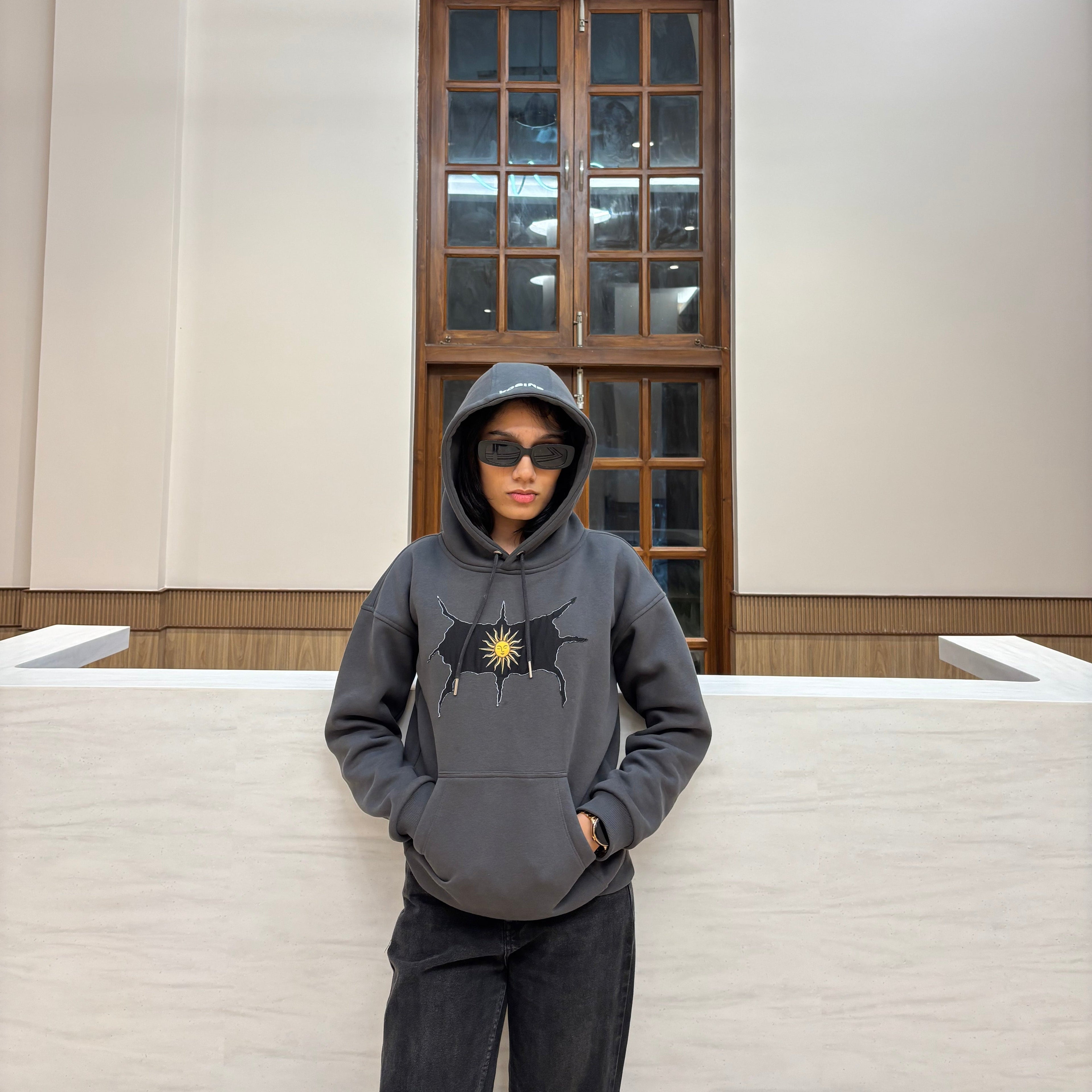 Person wearing a gray hoodie with a logo in a room with a large mirror.