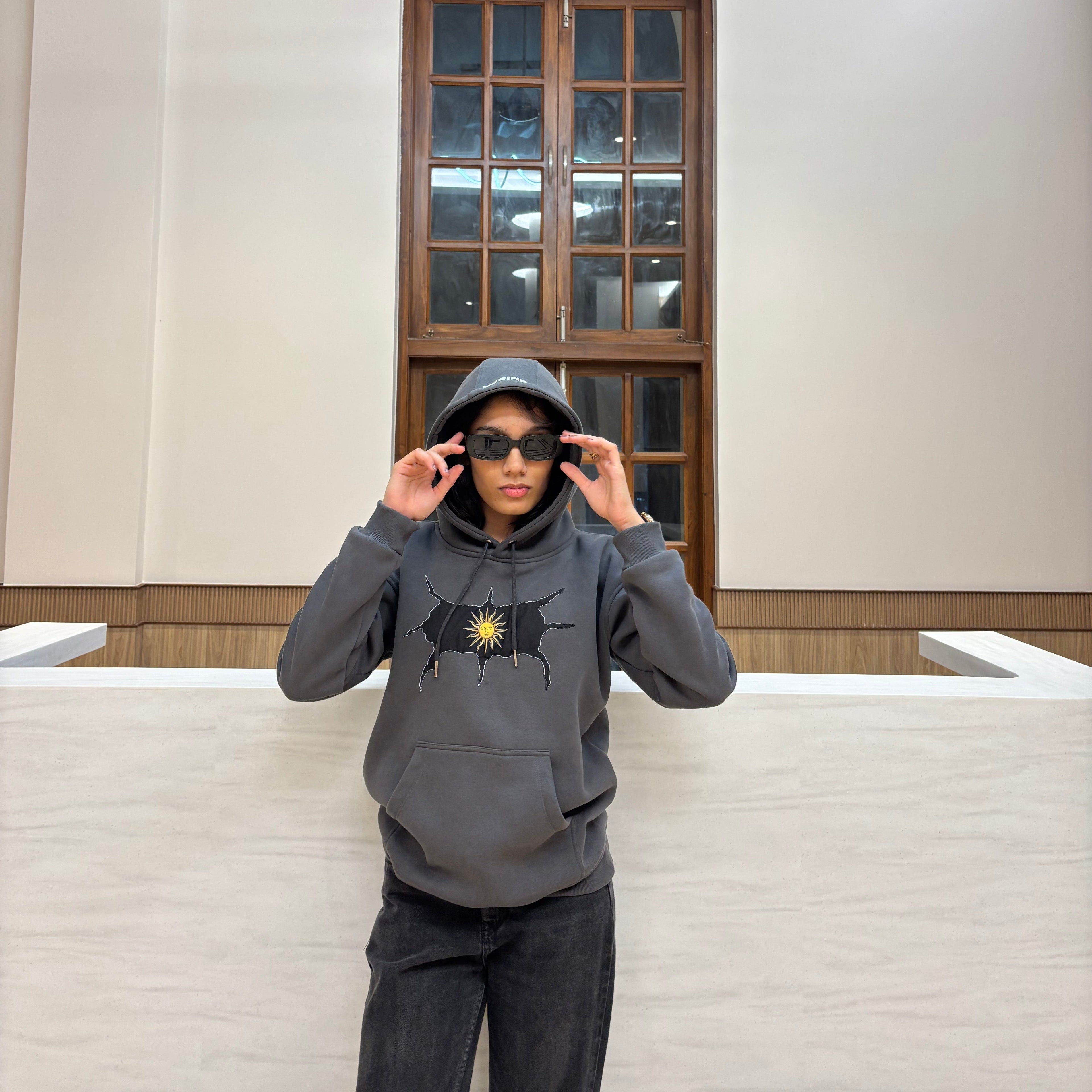 Person wearing a gray hoodie with a star design, standing in a room with a wooden door and white walls.